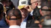 Vice-President Mike Pence tries on a fan's Caterpillar hat while shaking hands with employees during visit.